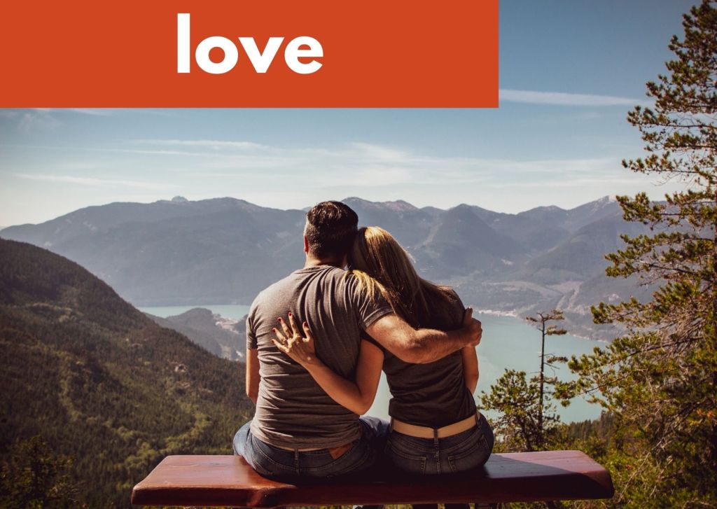 a couple sitting on a bench with arms around each other looking at a mountain view and the word love
